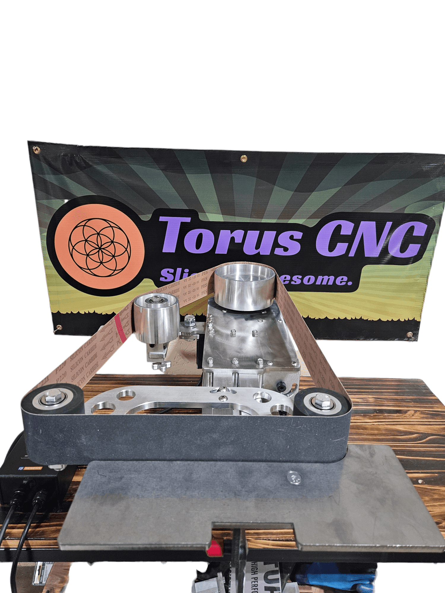 Front-on photo of a Torus CNC 2x72 belt grinder with a P220 silicon carbide belt installed, shop banner behind it