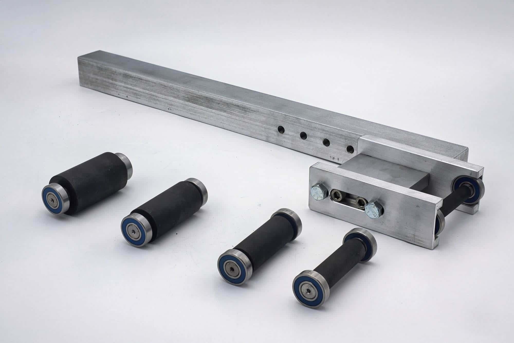Aluminum bracket, drilled mounting plate, and five rubber-coated idler rollers arranged on a table