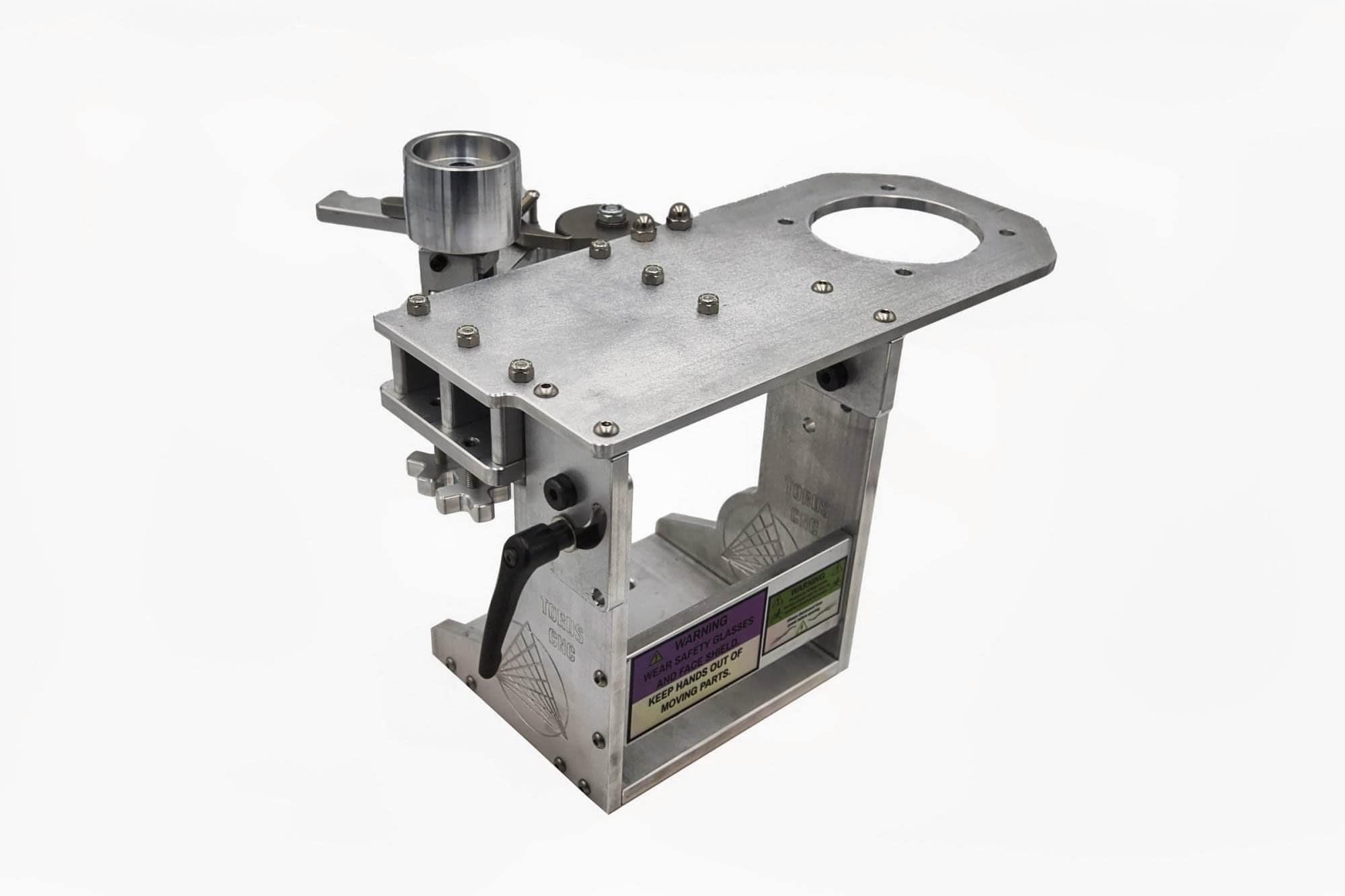 Machined aluminum grinder base with a top plate, black cam lever, warning labels and a wheel on a bracket, on white