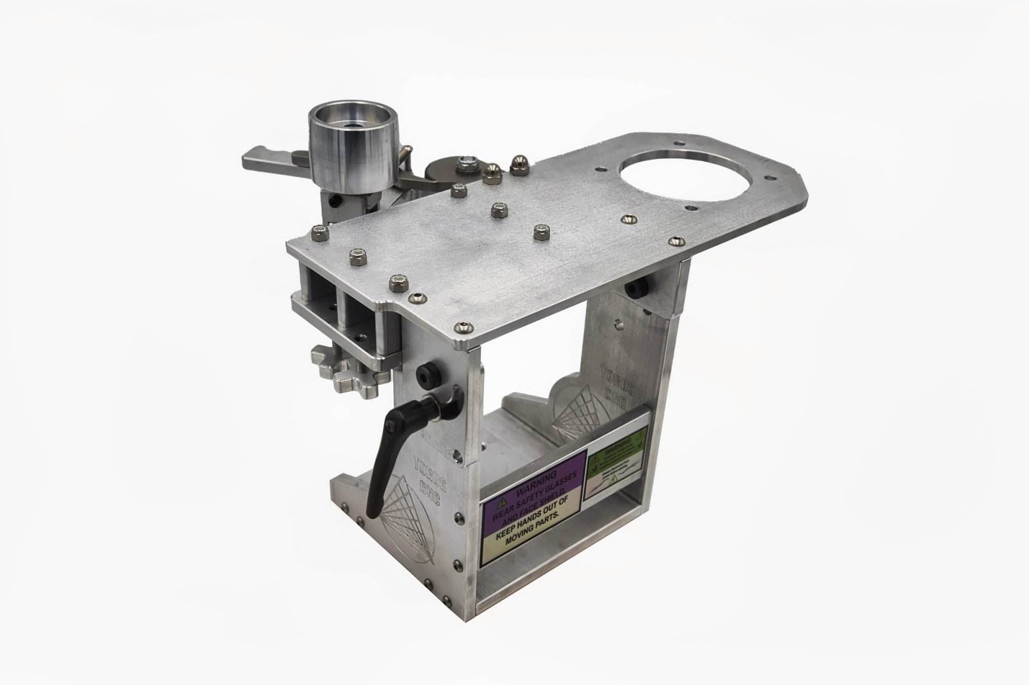 Machined aluminum grinder base with a top plate, black cam lever, warning labels and a wheel on a bracket, on white