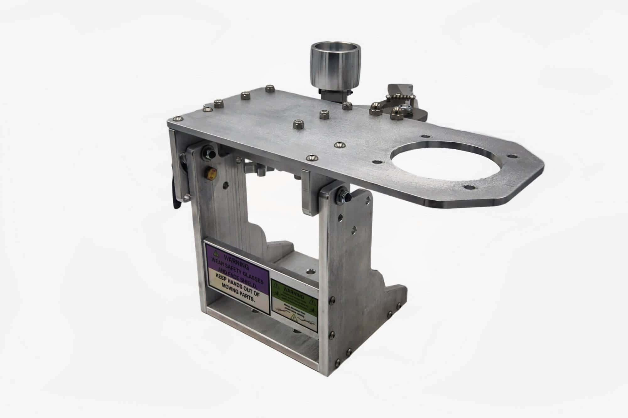 Aluminum tool arm mounting plate lying flat with a large pivot bore, mounting bolts, and safety warning labels on the upright base