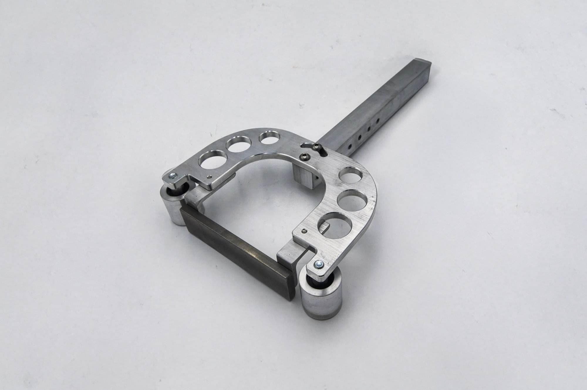 Machined horseshoe-shaped bracket with mounting holes and dual roller bearings for a grinder arm