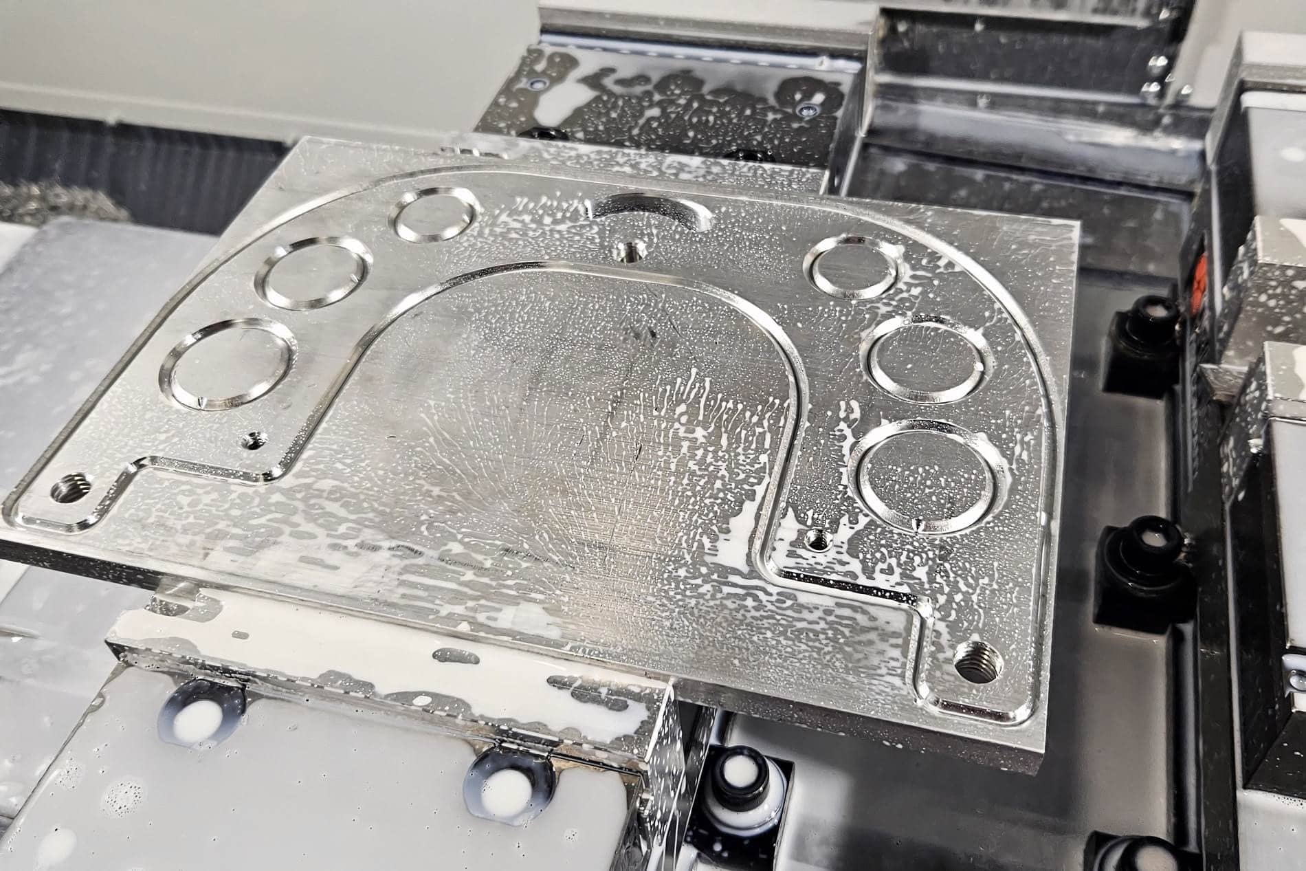 A freshly machined aluminum grinder plate, still wet with coolant, on the HAAS mill table