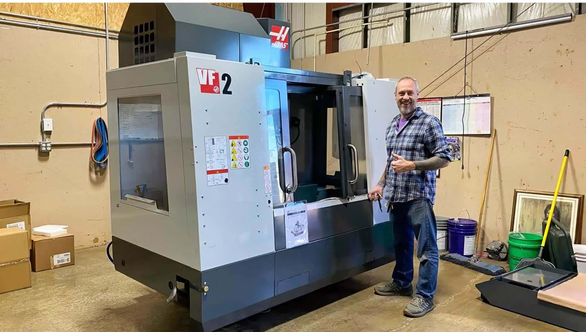 Torus CNC team member giving a thumbs up beside a new Haas VF-2 CNC milling machine