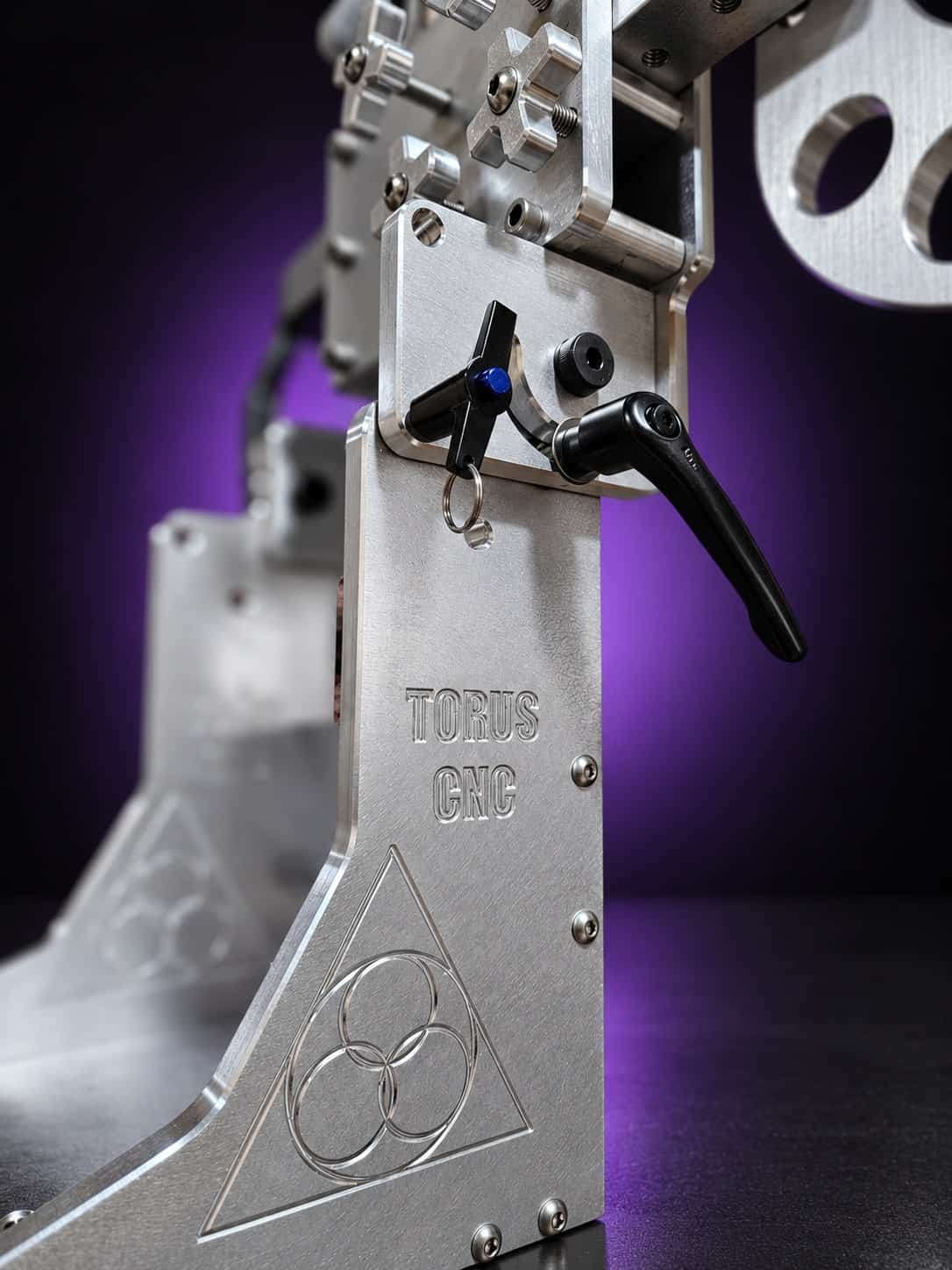 Classic grinder base upright with engraved Torus CNC logo, black cam lever and knob, close-up, on black with a purple glow