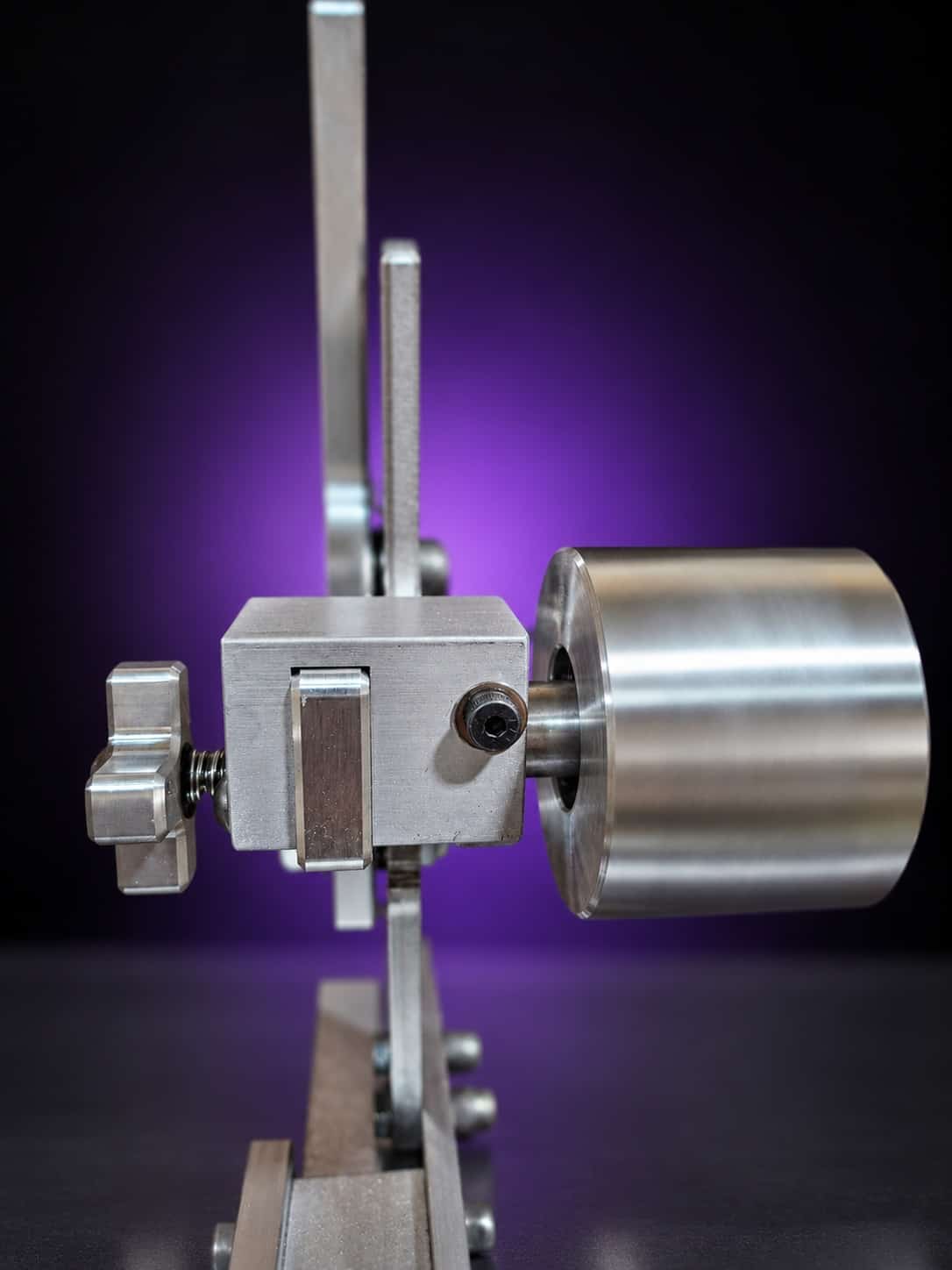 Classic grinder tracking block with star knob and a wide aluminum idler wheel, close-up, on black with a purple glow