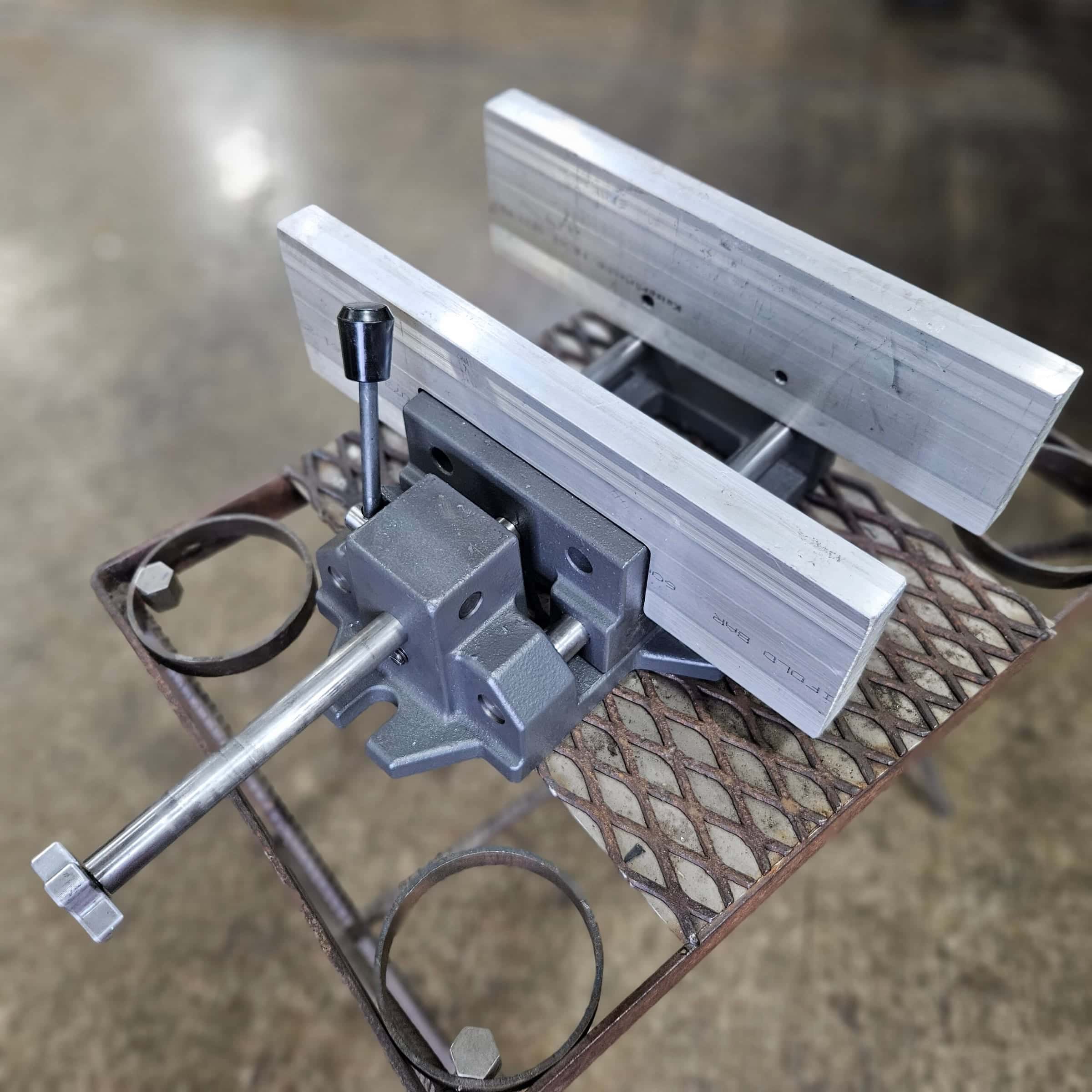 Close-up of a Torus CNC quench vise handle and clamp holding aluminum bar stock