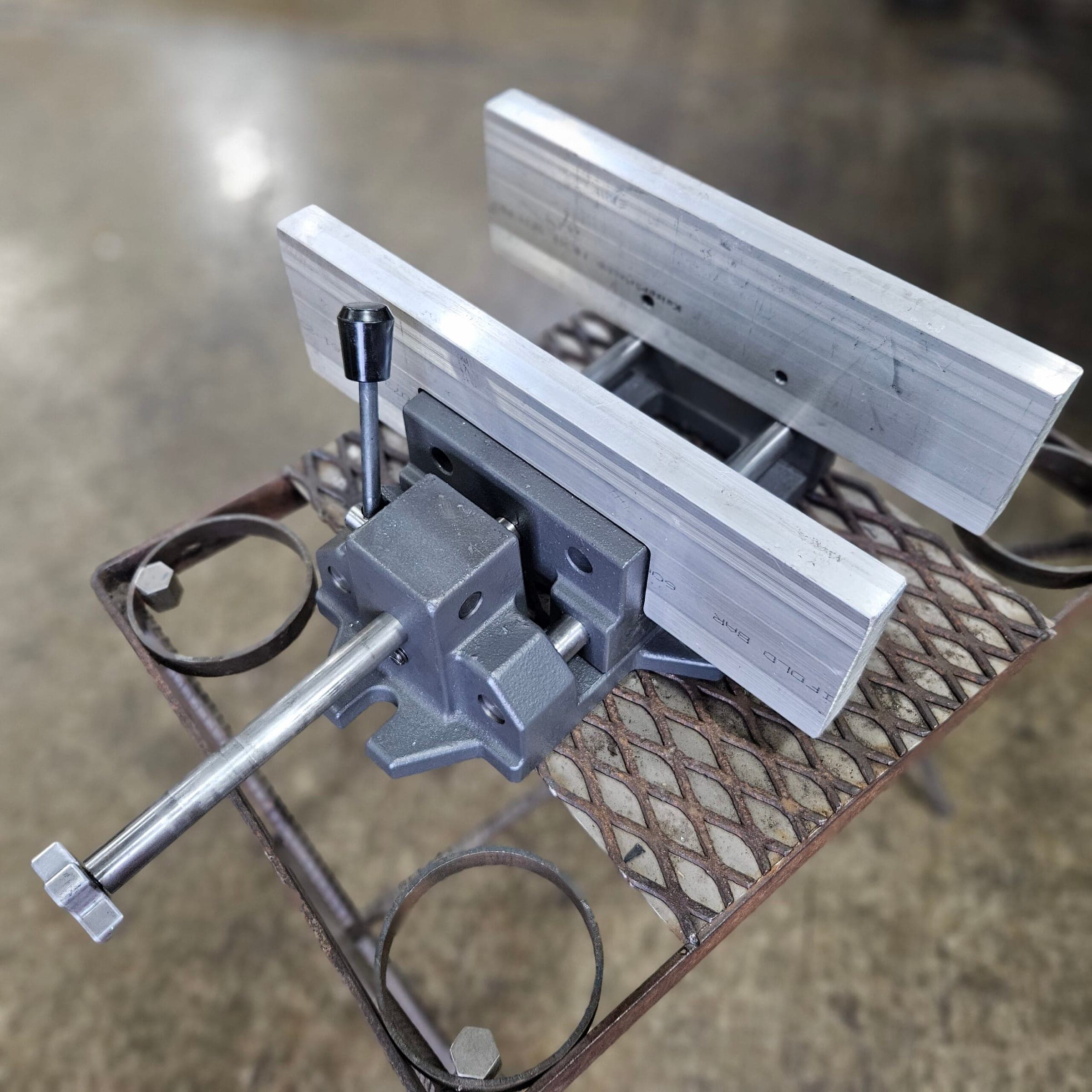 Close-up of a Torus CNC quench vise handle and clamp holding aluminum bar stock