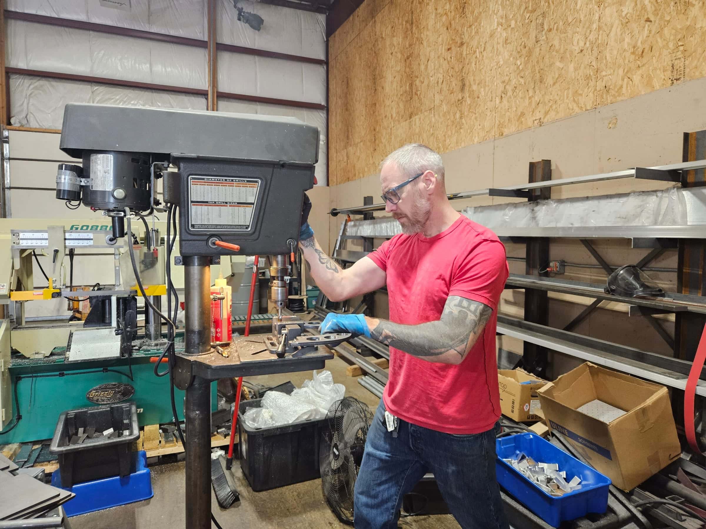 Rich Linville in safety glasses drilling a bracket at the drill press in the Sterling shop