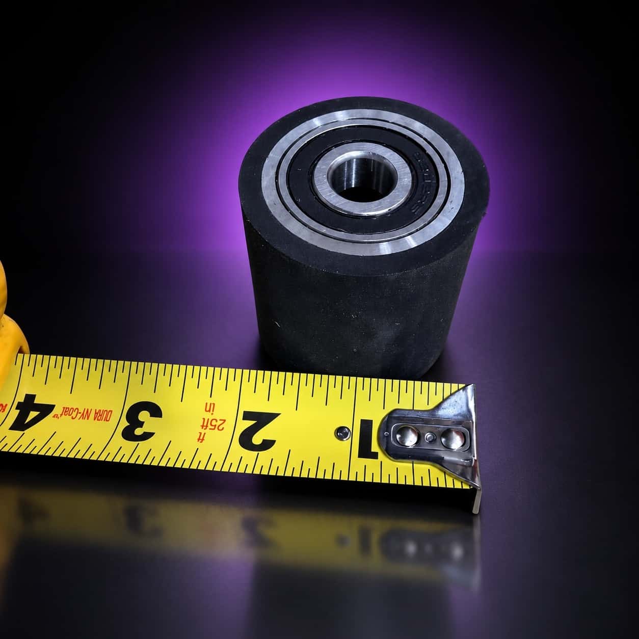 2-inch rubber flat-platen wheel standing bearing face up beside a tape measure for scale, on black with a purple glow