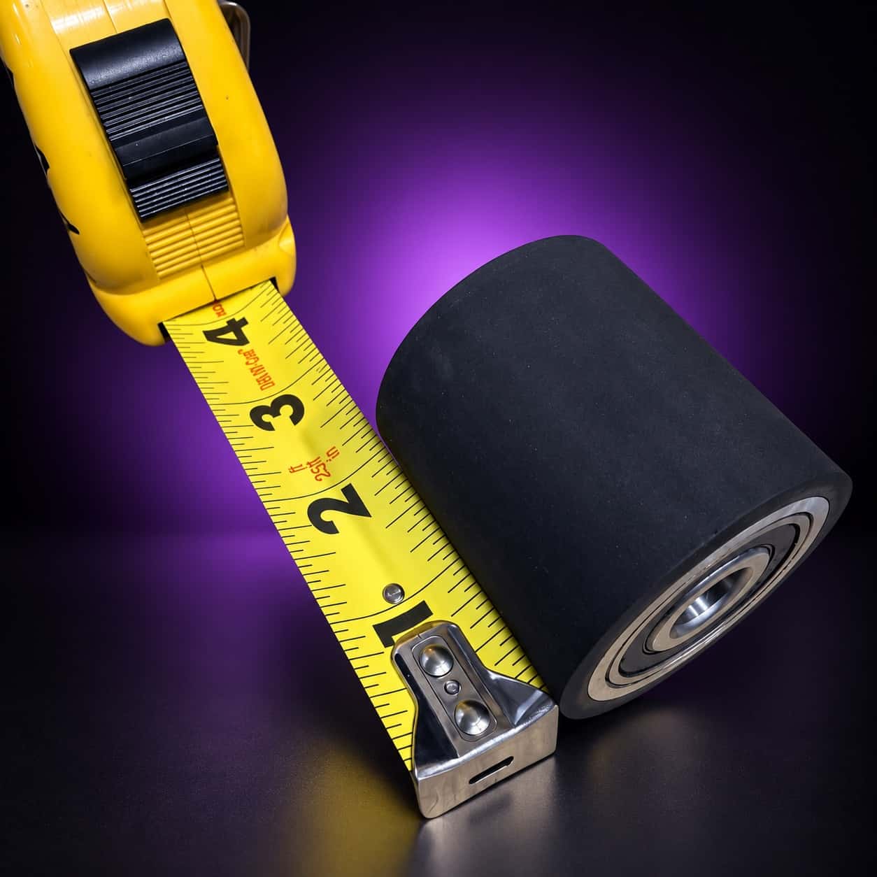 2-inch rubber flat-platen wheel on its side, tread and bearing showing, tape measure at left, on black with a purple glow