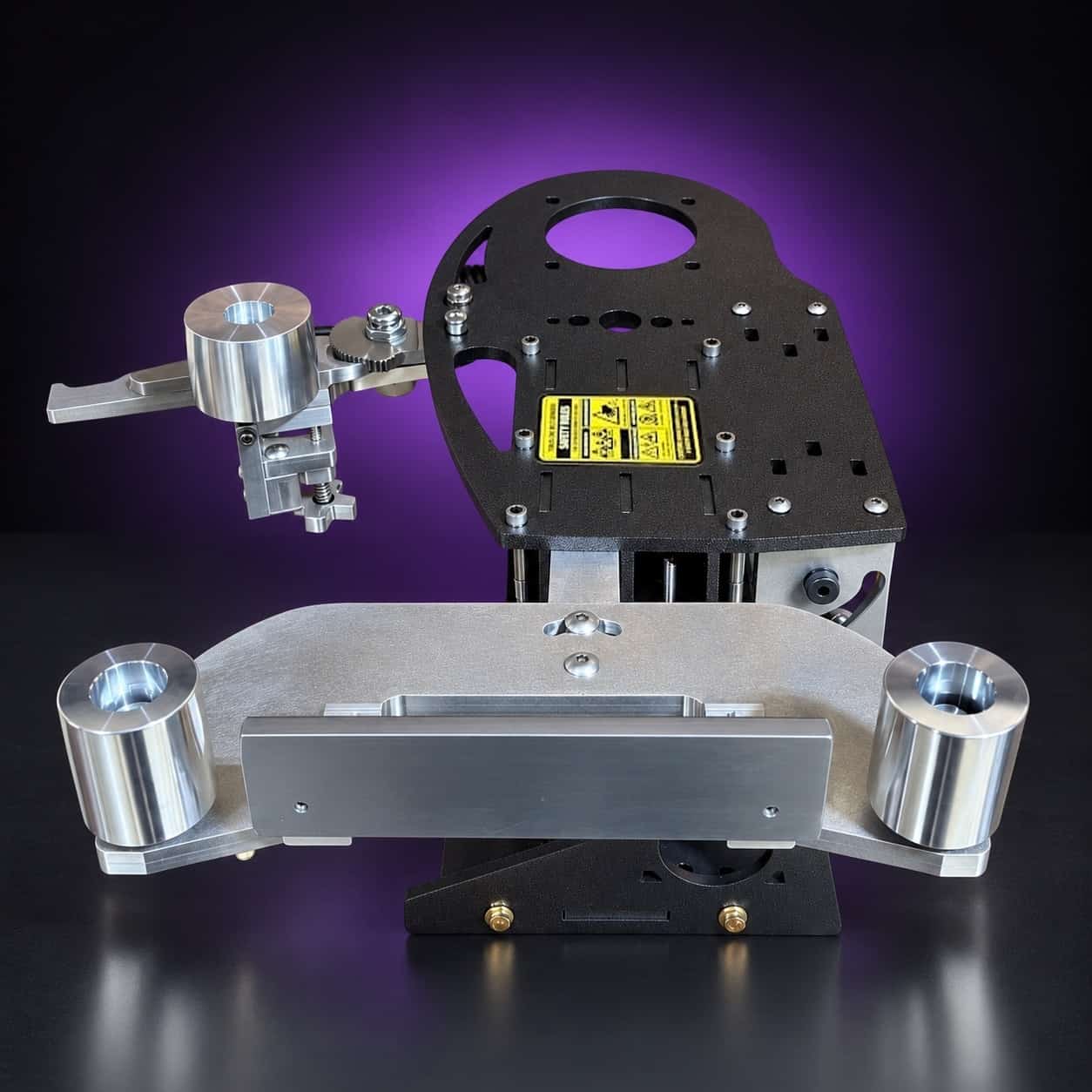 Nebula laid horizontal, elevated three-quarter view: aluminum arm with two idler wheels in front, on black with a purple glow