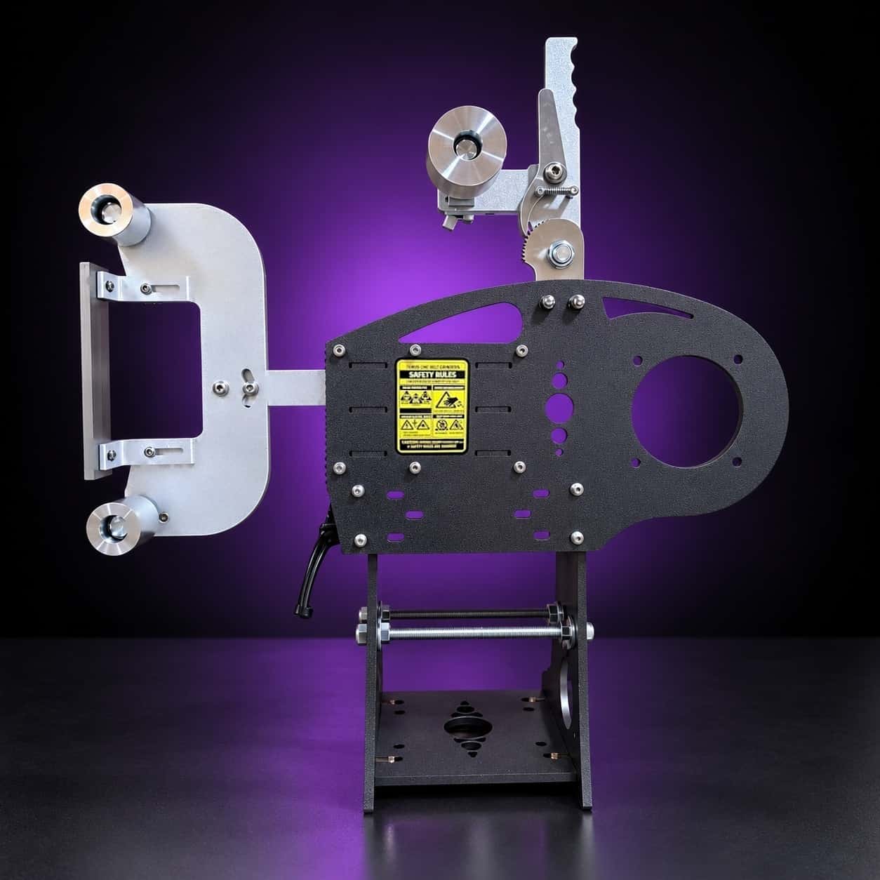 Nebula 2x72 grinder, side view with Safety Rules label, threaded cross rods and black base, on black with a purple glow