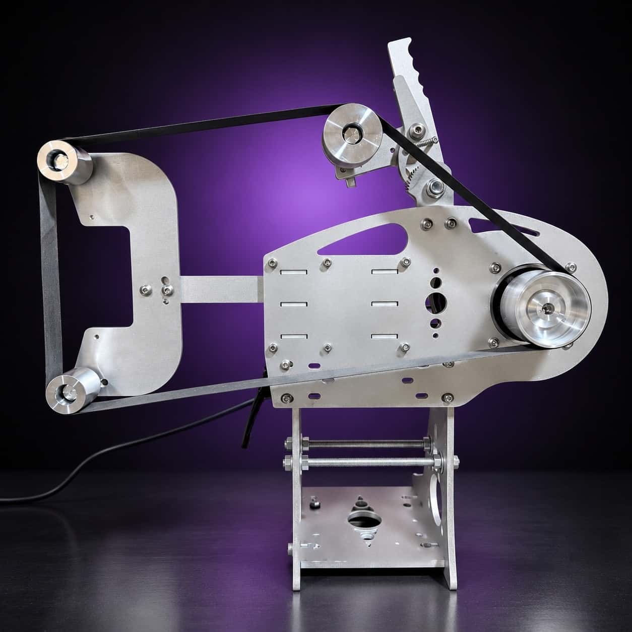 Nova aluminum 2x72 grinder with flat-platen tool arm and belt fitted, side view, on black with a purple glow